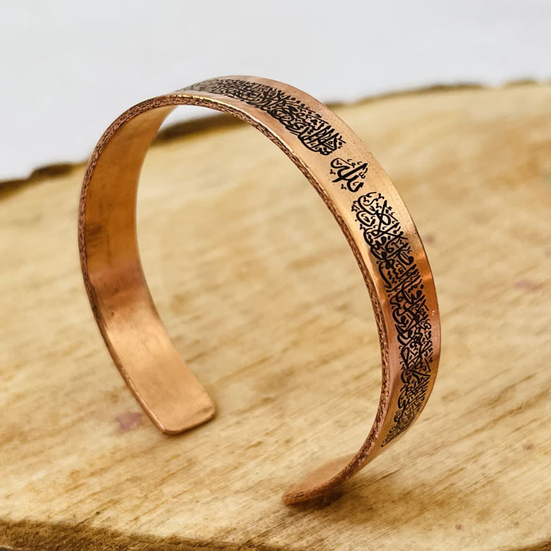 Copper cuff bracelet engraved with Quranic calligraphy on a white background